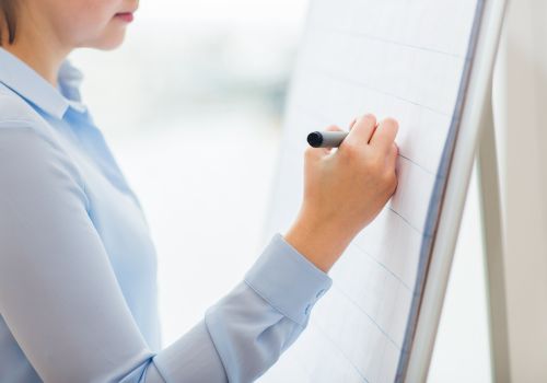 Person writing on a blank flip chart with a marker.